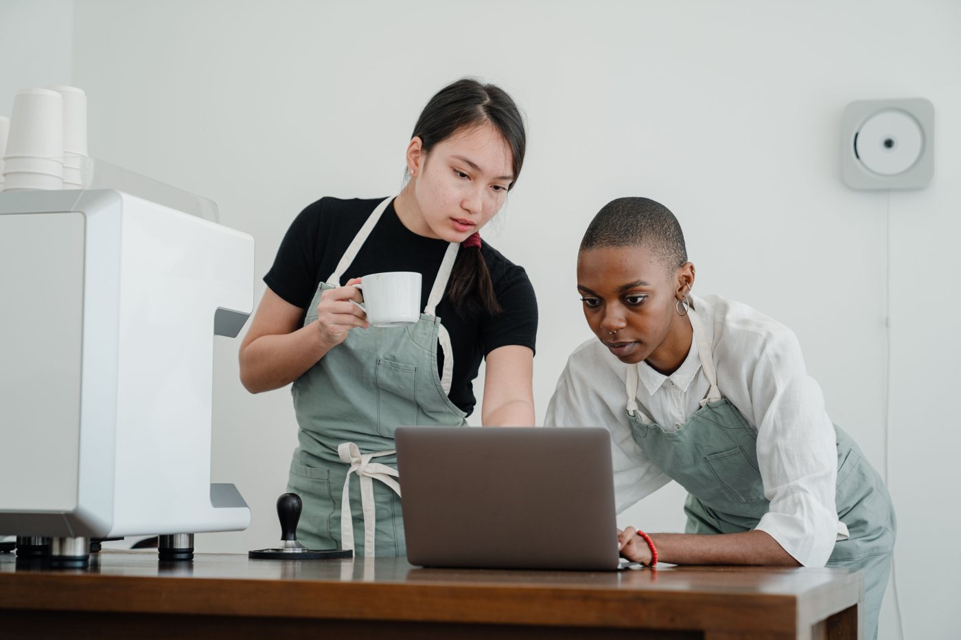 Two café colleagues in aprons reviewing a laptop behind a counter